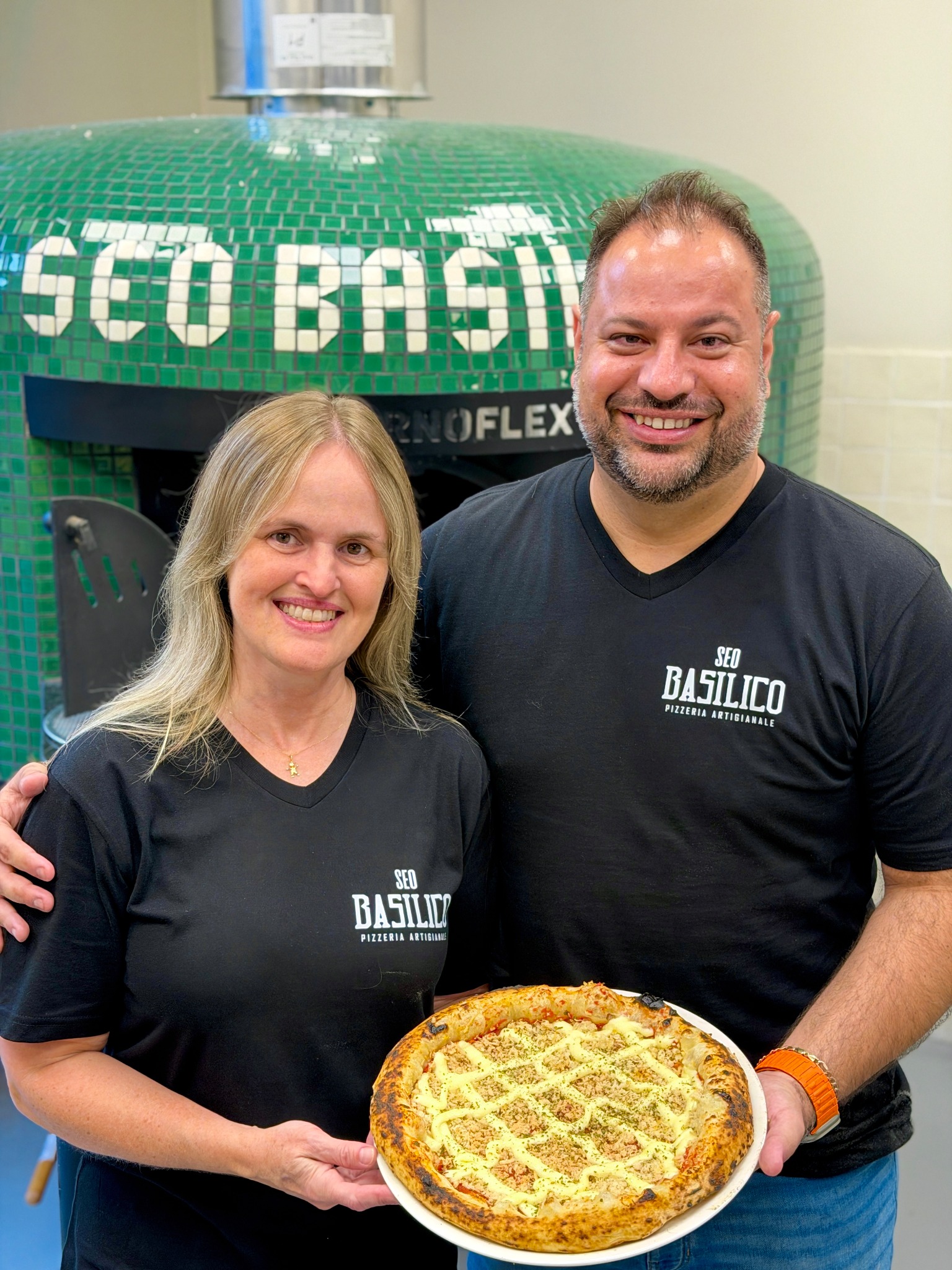 The Seo Basilico owners together, holding a pizza in front of their oven